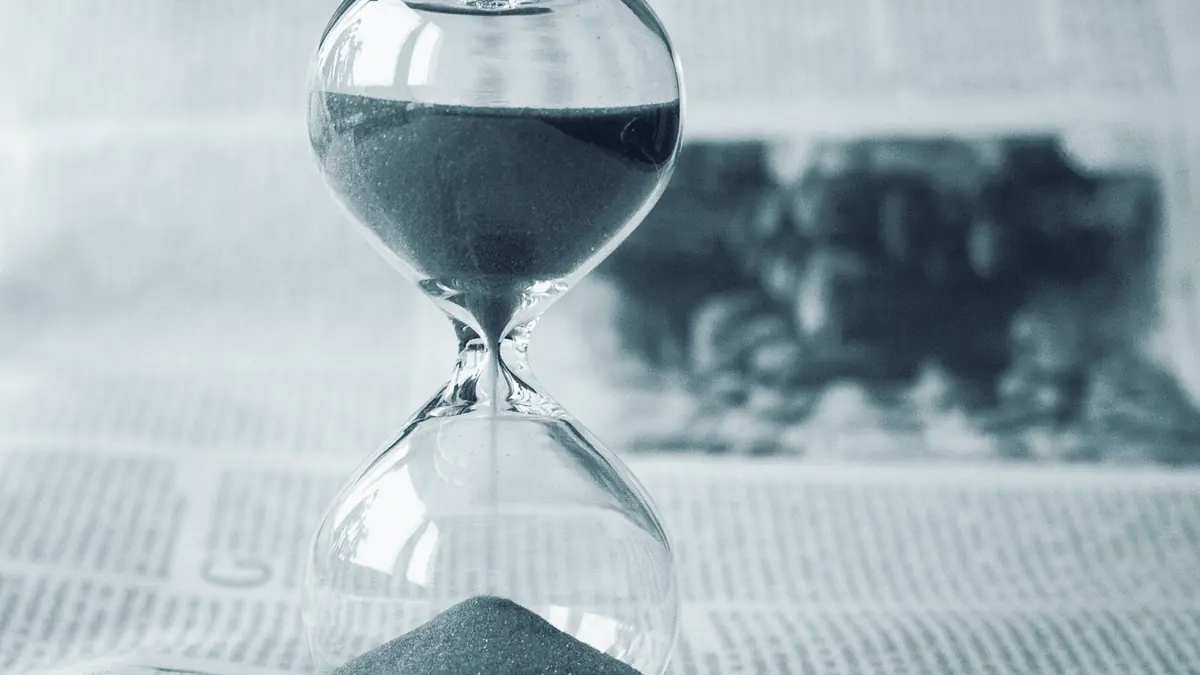 Sanduhr mit rotem Sand auf einer aufgeschlagenen Zeitung